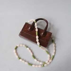 Vue détaillée de la bandoulière en perles acryliques rose et vert sur un sac à main marron