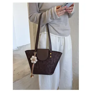Detailed view of a minimalist brown leather tote bag featuring a white floral charm accessory.