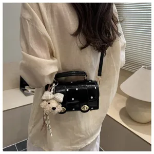 Detailed view of a small black polka dot pillow bag featuring a cute plush bear keychain charm