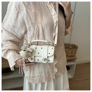 Detail of a stylish white polka dot pillow crossbody bag with a cute plush dog charm