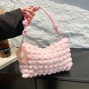 Trendy pink pleated smocked handbag with knotted strap and flower charm accessory.