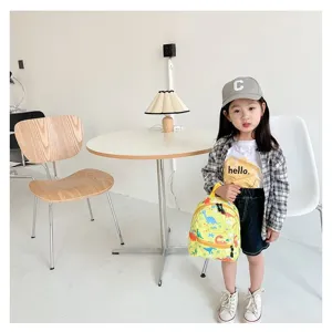 Toddler girl modeling a small yellow backpack with colorful dinosaur prints in a modern room