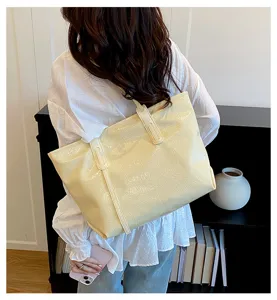 Detailed view of a cream glossy tote bag carried by a model in a casual commuter setting.