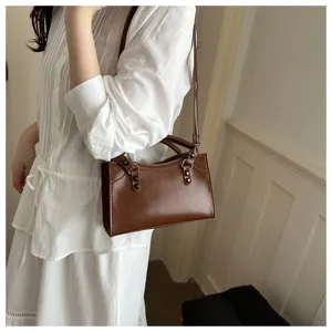 Vintage brown shoulder bag with rivet detail shown on model in a stylish white dress