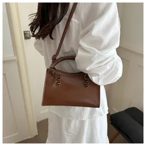 Detailed view of a vintage brown rivet motorcycle bag carried by a model in a white dress