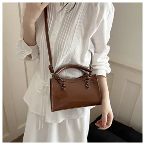 Close-up of a brown rivet locomotive crossbody bag worn with an elegant white dress