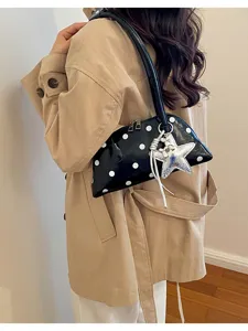 Stylish black bowling bag with white polka dots worn as a chic underarm handbag