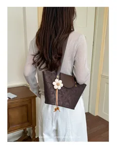Vista posteriore di una borsa tote marrone con ciondolo a fiore indossata da modella