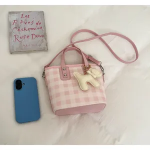 Detail view of pink and white gingham bucket bag with a cute cream-colored dog charm