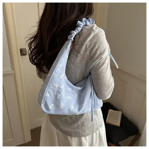 Detail of a blue and white gingham underarm tote bag with white bow prints and ruched strap.