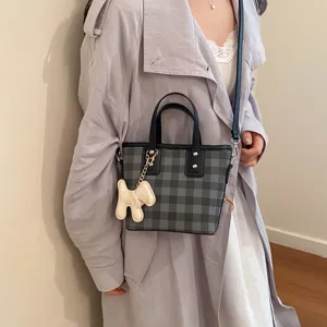 Detailed view of a stylish grey checkered bucket bag featuring a cute puppy charm