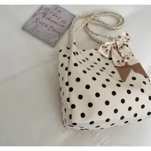 Detailansicht einer cremefarbenen Polka-Dot-Einkaufstasche mit Seidenschal und geflochtenen Riemen.