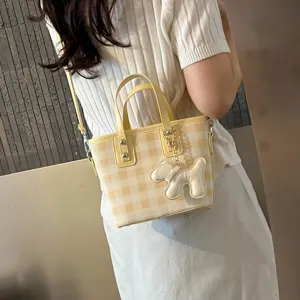 Close-up detail of yellow checkered bucket bag with cute dog charm shown on a model