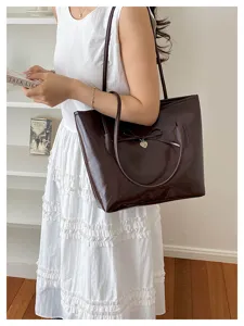 Lifestyle view of a brown faux leather shoulder bag with a bow and heart charm.