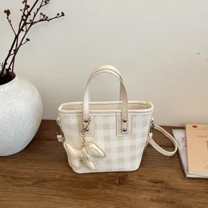 Detailed view of beige checkered bucket bag with cute dog charm on wooden table