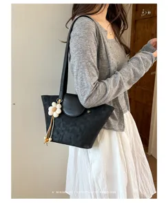 Borsa a spalla nera testurizzata minimalista indossata con cardigan grigio e gonna bianca.