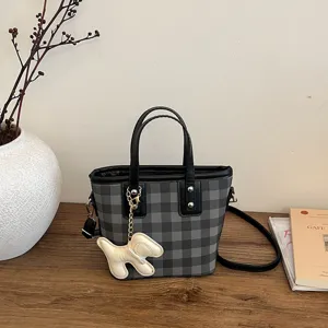 Detailed view of a stylish grey checkered bucket bag featuring a cute white dog accessory charm