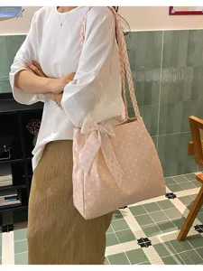 Lifestyle-Ansicht einer rosa gepunkteten Tragetasche mit Schleife und Flechtriemen.