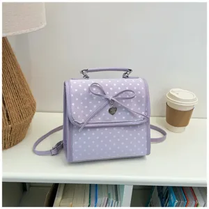Detail of a lavender polka dot backpack with a bow and heart charm on a desk.