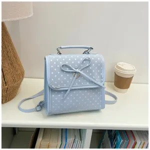 Elegant light blue polka dot backpack with a cute bow detail on a clean white desk