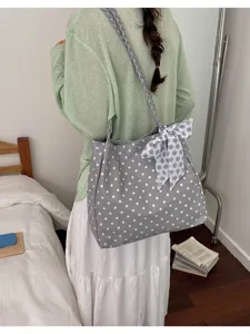 Lifestyle shot of a gray polka dot tote bag with a floral bow on a model's shoulder.