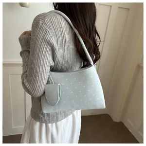 Vista detallada del bolso de hombro azul claro con lunares y bolsa pequeña en un modelo