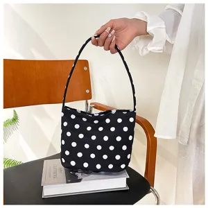 Vista detallada de un elegante bolso negro con lunares blancos sostenido sobre una silla