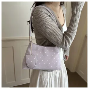 Vista detallada de bolso de hombro lavanda con lunares y pequeño estuche en una modelo