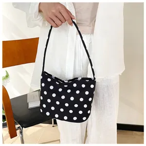 Primer plano de un bolso hobo con lunares blancos y negros sostenido por una modelo.