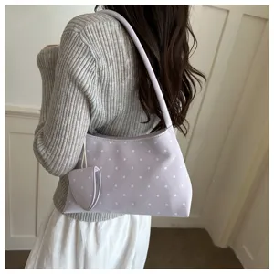 Detalle de un bolso de hombro lavanda con lunares y un monedero en forma de corazón.