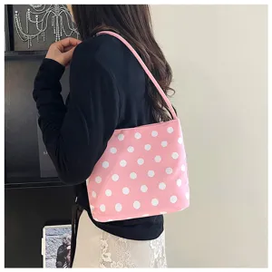 Detalle de un bolso rosa con lunares blancos llevado al hombro por una modelo joven