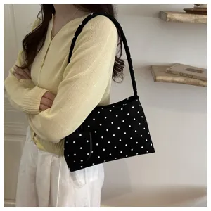 Elegante bolso de hombro negro con lunares mostrado por una modelo en ambiente hogar