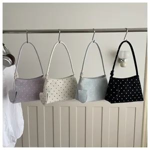 Cuatro elegantes bolsos de hombro con lunares en varios colores colgados en un perchero.