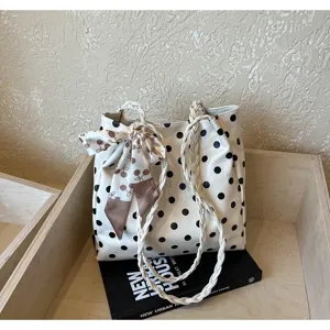 Detailed view of a white polka dot tote bag with braided handles and decorative scarf.