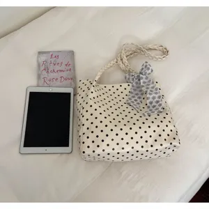 Cream polka dot tote bag with braided handles and floral bow next to a tablet