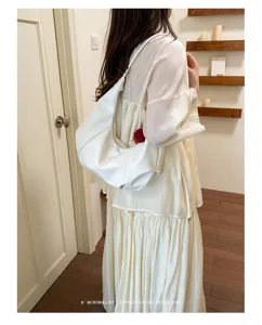 White minimalist dumpling hobo bag shown being worn by a model in a cozy interior setting.