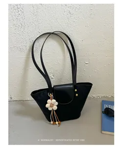 Dettaglio di una borsa a secchiello nera minimalista con ciondolo a fiore bianco.