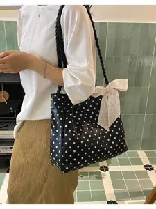 Detail view of black polka dot tote bag with bow charm on model's shoulder.