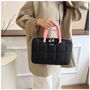 Borsa porta PC nera trapuntata con manici rosa portata da una donna in beige.
