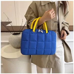 Borsa trapuntata blu per laptop con manici gialli portata da una modella in cappotto