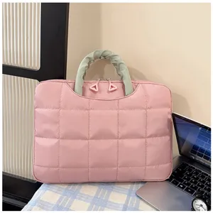 Dettaglio borsa per laptop trapuntata rosa con manico verde unico accanto al computer