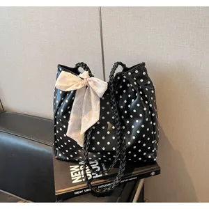 Close-up of black polka dot tote bag with pink floral bow and braided handles