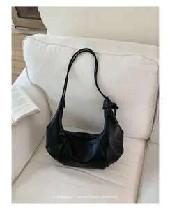 Minimalist black leather dumpling shoulder bag on a white sofa in a cozy interior setting