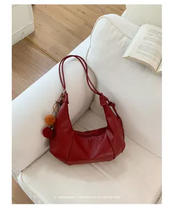 Close-up of a red retro minimalist hobo bag with pom-pom charms on a white sofa.