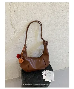 Sophisticated retro brown pleated hobo bag with a pom-pom charm on a minimalist pedestal