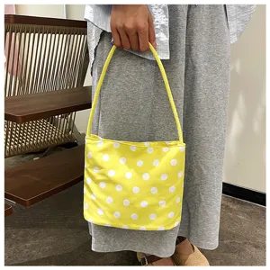 Bolso tote amarillo con lunares blancos llevado por persona con vestido gris y zapatos