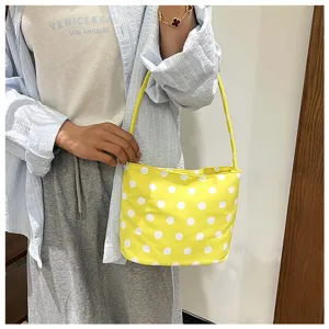 Bolso de cubo amarillo con lunares blancos llevado por una modelo en estilo casual.