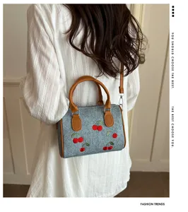 Close-up detail of a fashion cherry embroidered denim shoulder bag worn by a model