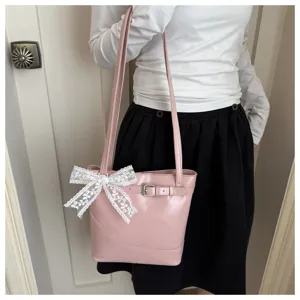 Dettaglio borsa a secchiello in pelle rosa con fiocco in pizzo bianco e fibbia.