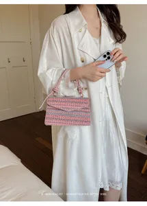 Primo piano di una borsa a mano quadrata intrecciata rosa tenuta da una modella